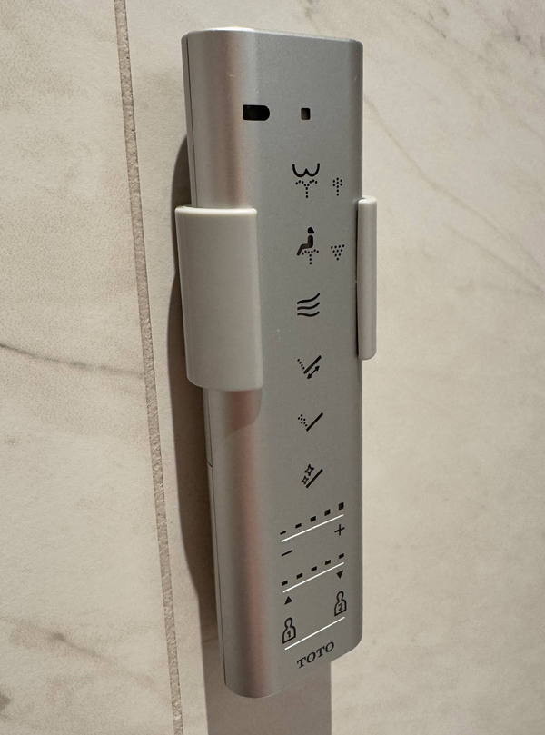 A grey remote control, mounted to a marble-tiled wall.