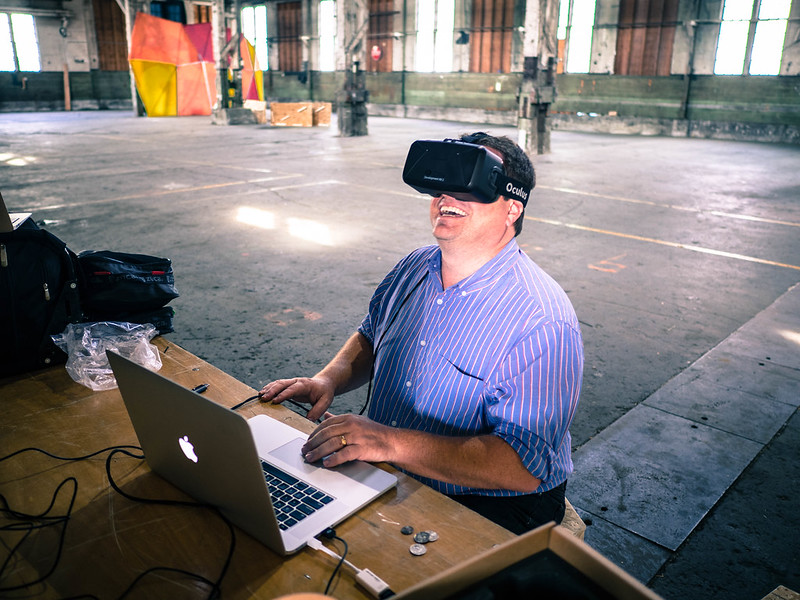 The author, wearing a VR headset and smiling. He is seated at a desk, but fully clothed and both hands are visible.